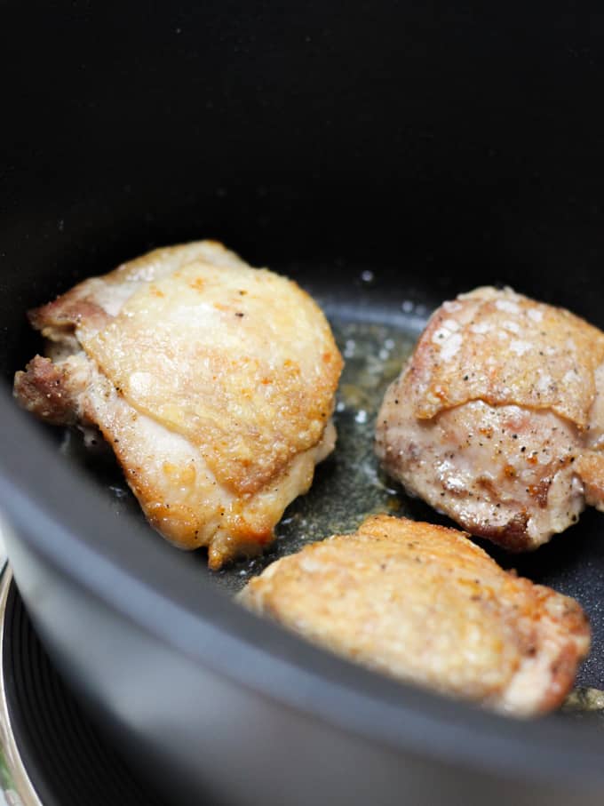 Browning chicken thighs in a black slow cooker for a recipe.