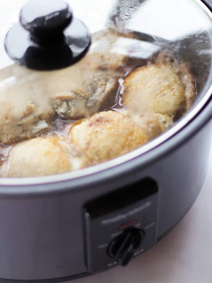 Lid on crock pot slow cooker showing chicken thighs cooking.