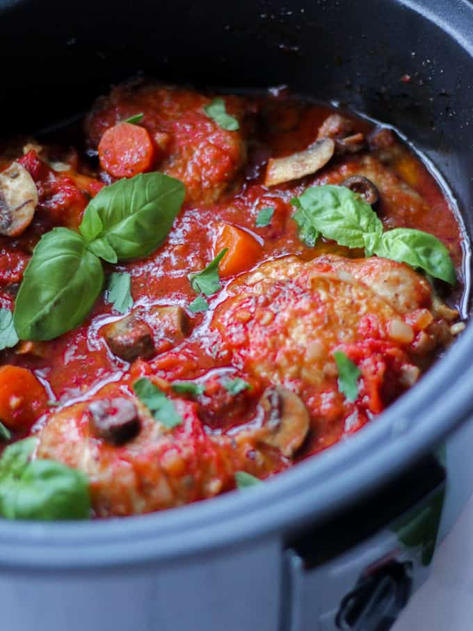 Side view of slow cooker chicken cacciatore with tomatoes and basil leaves.