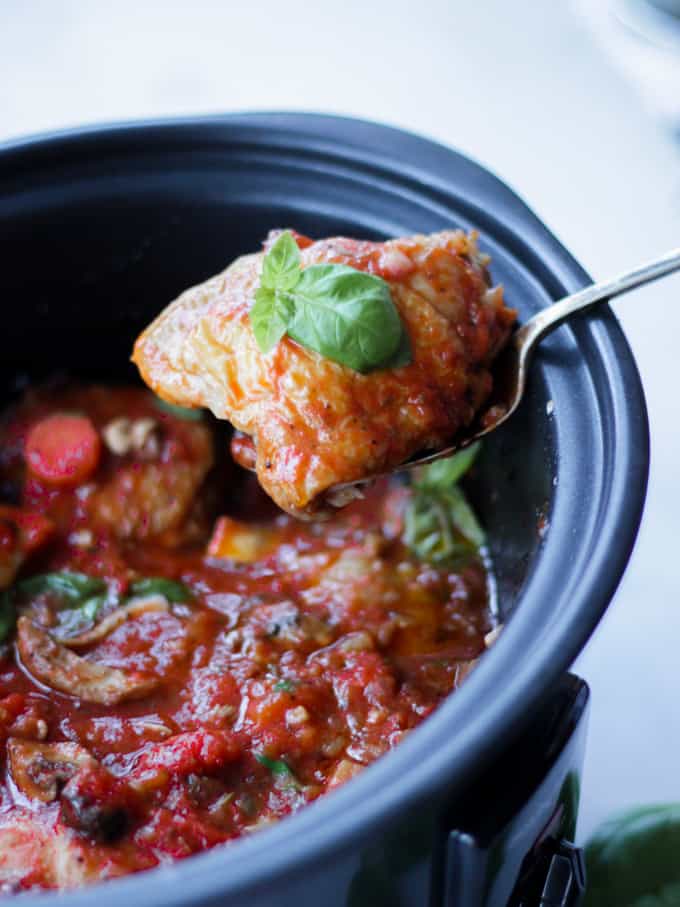 Cooked chicken thigh lifted from a slow cooker chicken cacciatore, with basil leaf on top.