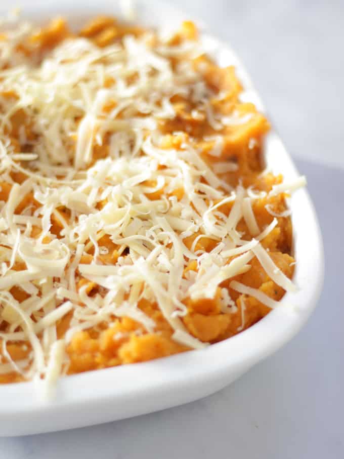 Mashed sweet potato in a white dish topped with cheese grated on a white background for Sweet Potato Cottage Pie recipe.