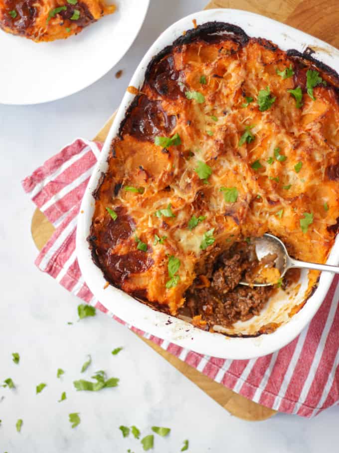 Overhead photo of sweet potato cottage pie with a spoonful taken out on a red and white fabric.