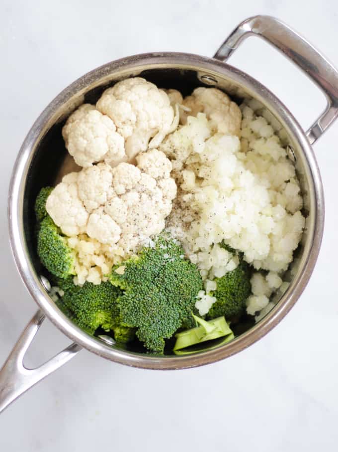 Pan of vegetables to make broccoli and cauliflower soup with cheddar cheese recipe before cooking on white marble background.