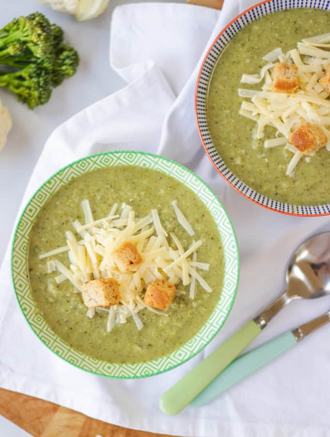 Overhead shot of broccoli and cauliflower soup topped with cheese and croutons in a green bowl.