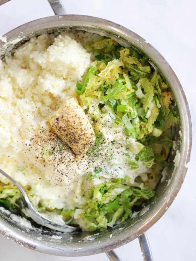 Colcannon ingredients in a silver saucepan, cabbage, spring onions (scallions), cream, butter, mashed potatoes salt and pepper on white background.