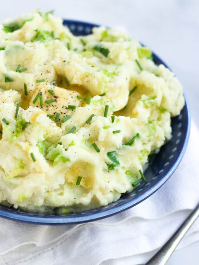 Side view of colcannon in a blue bowl on white background.