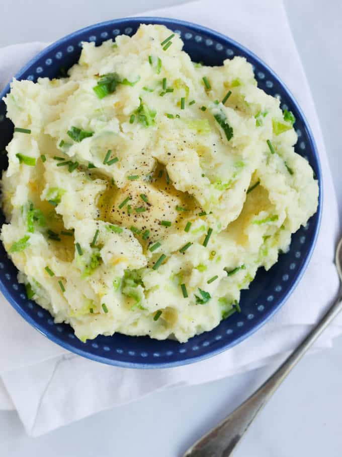 Overhead view of colcannon in a blue bowl on white background.