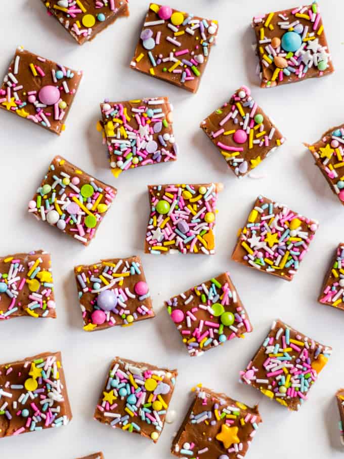 Cubes of homemade chocolate candy with colourful sprinkles on a white marble background.