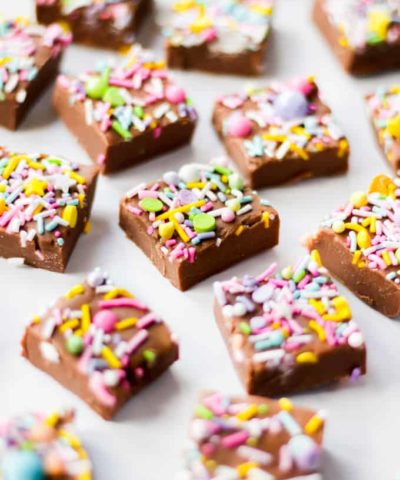 Cubes of milk chocolate microwave fudge with brightly coloured sprinkles on top, side view.