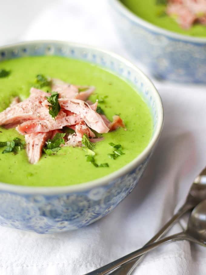 Blue bowl with pea and ham soup with mint and shredded ham in.