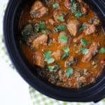 Overhead photo of beef spinach slow cooker curry in black slow cooker with green check cloth.