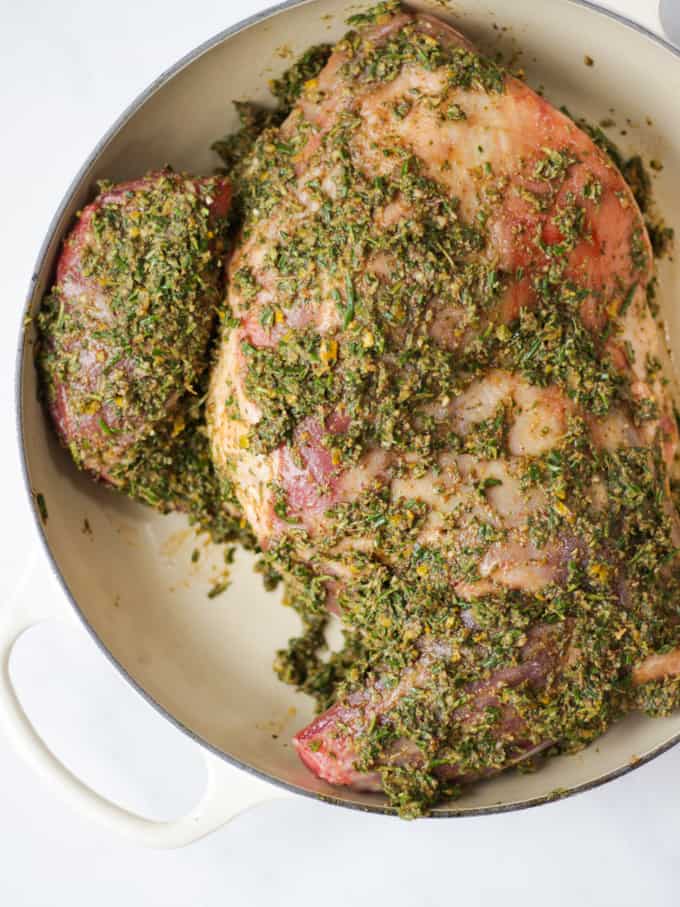 Raw herb coated shoulder of lamb ready for slow roasted shoulder of lamb in almond Le Creuset dish. 