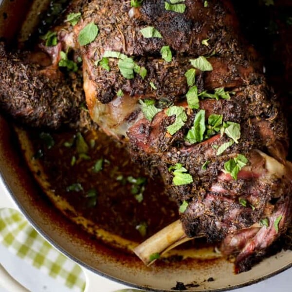 Close up of slow roasted shoulder of lamb with herb crust in almond Le Creuset casserole and green check tea towel.
