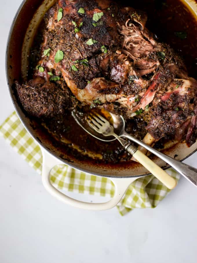 Overhead slow cooked lamb shoulder dish with green check cloth and marble background.