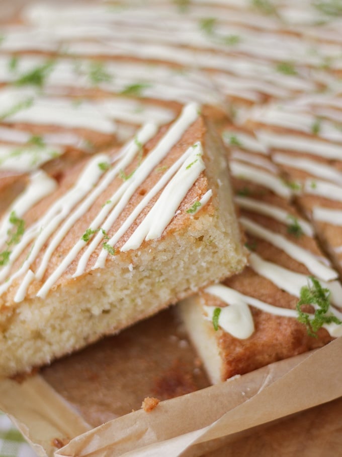 Side view of a gin and tonic cake bar topped with white chocolate drizzle and lime on baking paper.