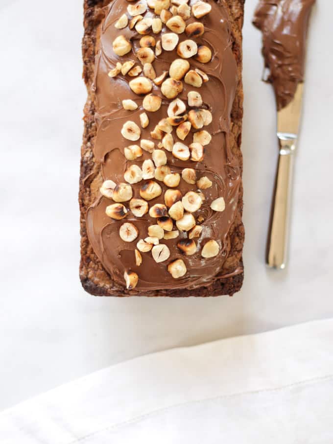 Overhead shot of Nutella Cake Loaf with knife on white background sprinkled with hazelnuts.