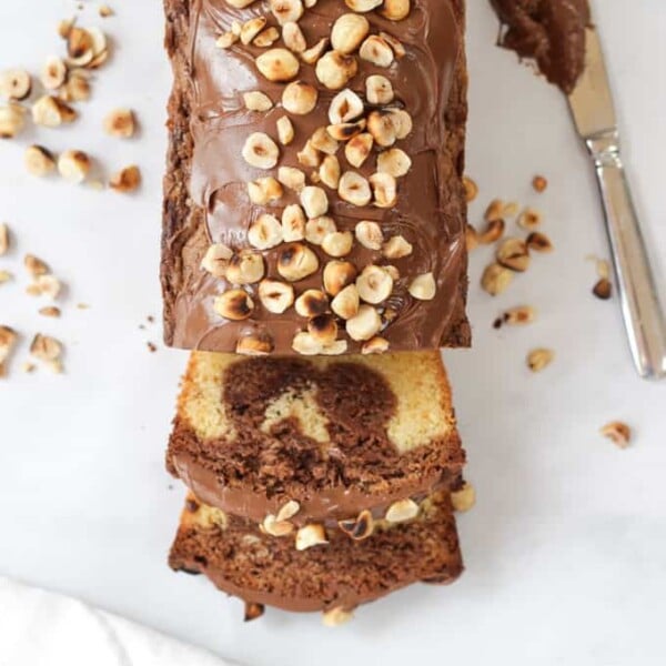 Overhead shot of slices Nutella Cake topped with hazelnuts on white marble background.