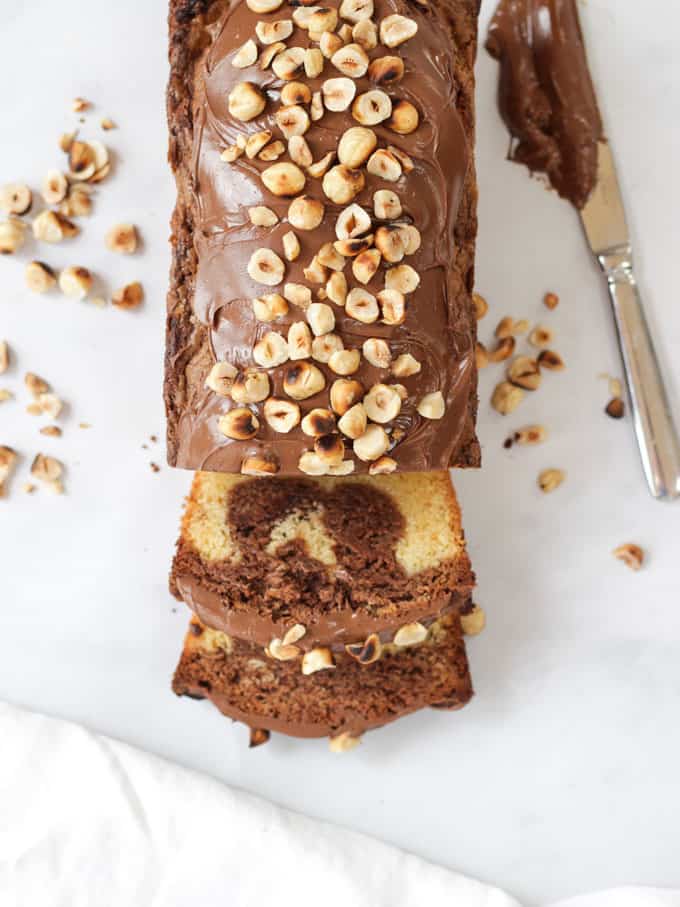 Overhead shot of slices Nutella Cake topped with hazelnuts on white marble background.