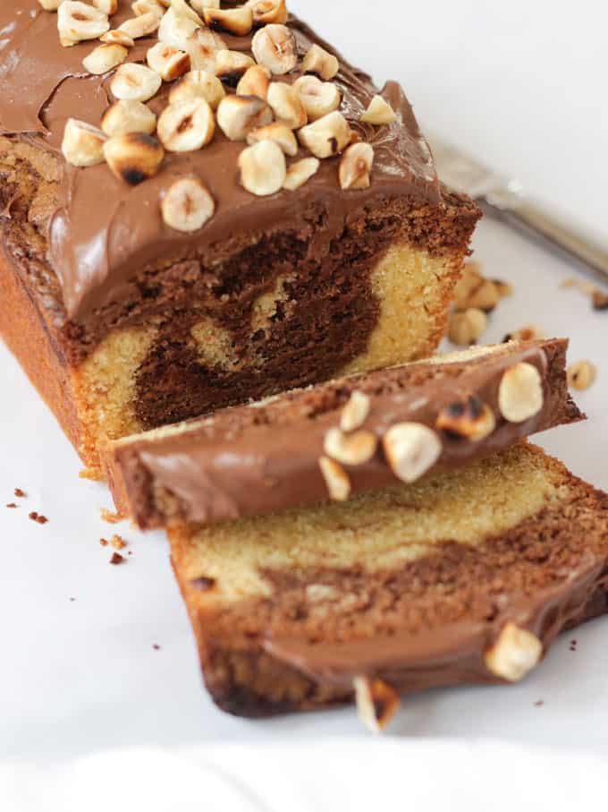Sliced Nutella Cake topped with Nutella and hazelnuts on white background
