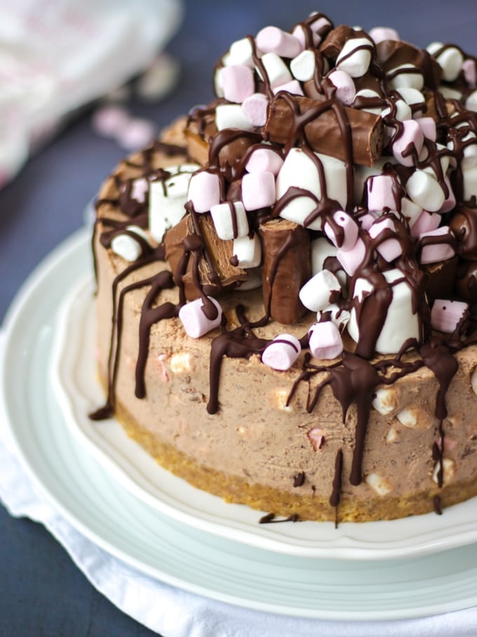 Chocolate cheesecake topped with marshmallows and drizzled dark chocolate on white plates on a grey background - Rocky Road Cheesecake.