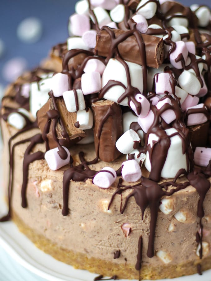 Close up photo of the top of a rocky road cheesecake no bake cheesecake recipe piled with marshmallows and drizzled with chocolate.