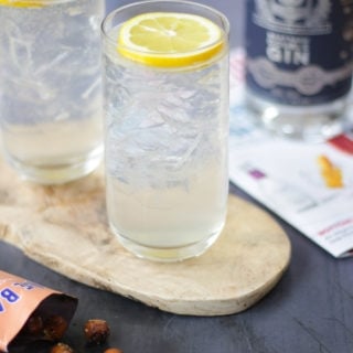 Two highball glasses filled with ice and a slice of lemon on top with gin fizz in the glass.