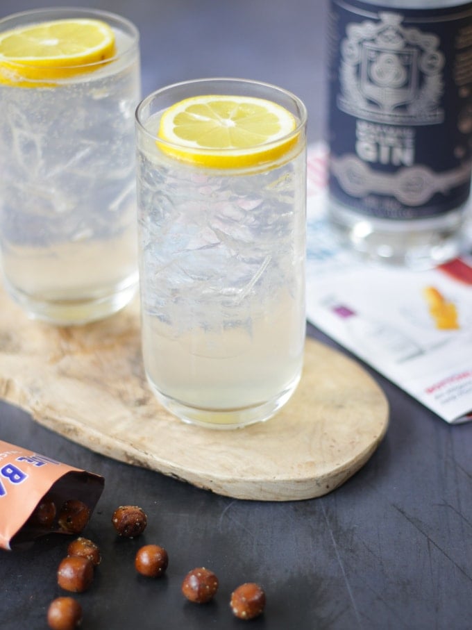 Two highball glasses filled with ice and a slice of lemon on top with gin fizz in the glass.