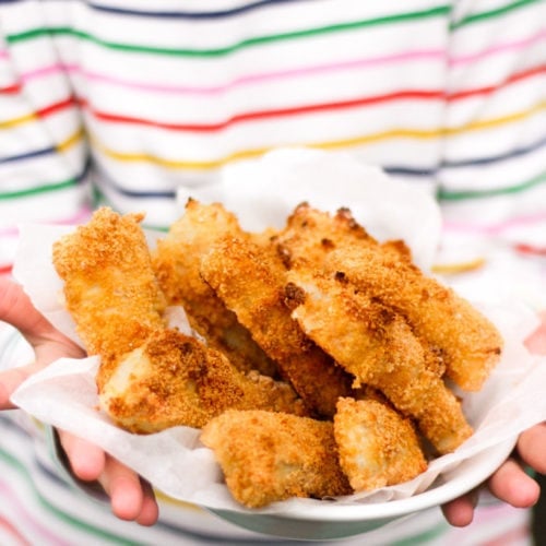 Close up of hands holding a bowl of homemade fish fingers with stripe t-shirt in the background. How to make easy peasy Homemade Fish Fingers using our simple recipe. Just four ingredients and supper tasty family meal every time. 