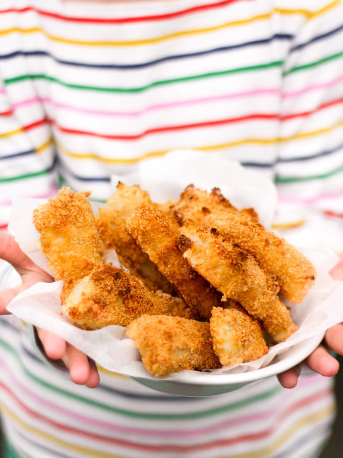 Close up of hands holding a bowl of homemade fish fingers with stripe t-shirt in the background. How to make easy peasy Homemade Fish Fingers using our simple recipe. Just four ingredients and supper tasty family meal every time. 