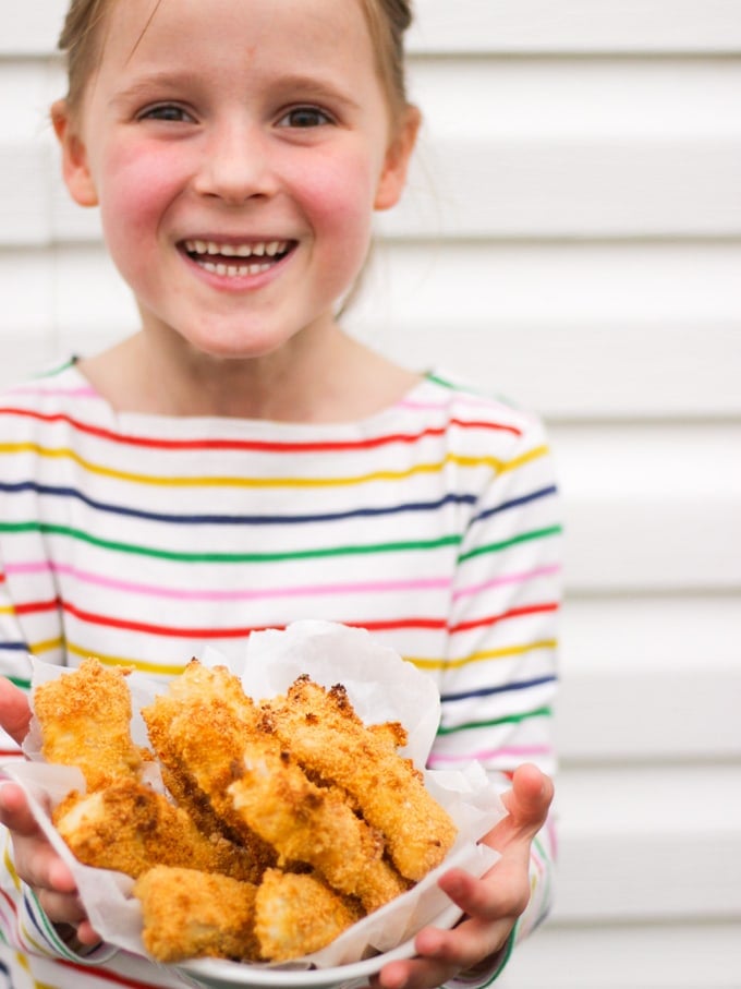 Girl in multi coloured strip t shirt holding a bowl of homemade fishfingers. How to make easy peasy Homemade Fish Fingers using our simple recipe. Just four ingredients and supper tasty family meal every time. 