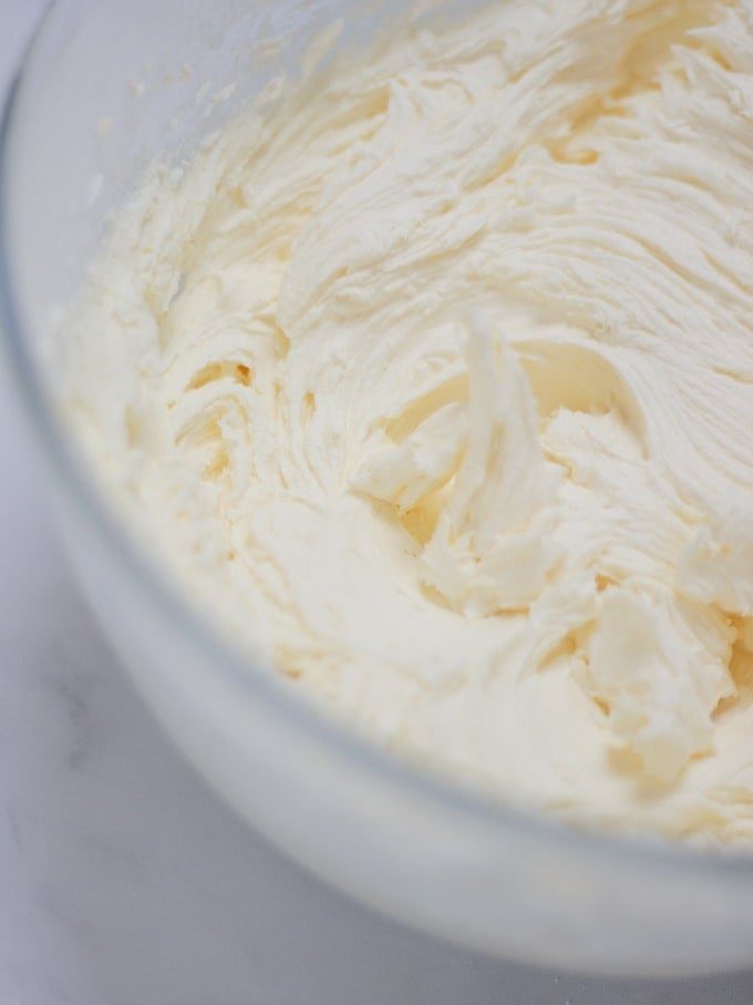 Bowl of buttercream icing frosting in a glass bowl for Pimms Cake recipe on white background.