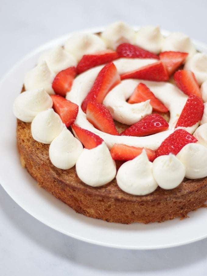 Layer of sponge cake covered with piped white buttercream icing and strawberries for Pimms layer cake recipe.