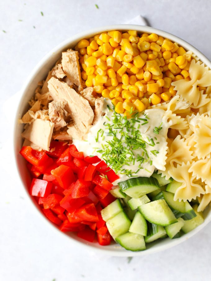 Sweetcorn, tuna, pasta, cucumber and peppers with dressing in a bowl.