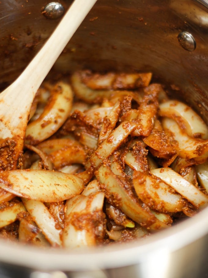 Onions cooking in a pan with spices with wooden spoon