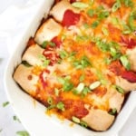 Overhead photo of chicken enchiladas in a white rectangular dish with tomato sauce, cheese melted, onions (scallions) and coriander (cilantro) for easy chicken enchiladas recipe which is also slimming world friendly.