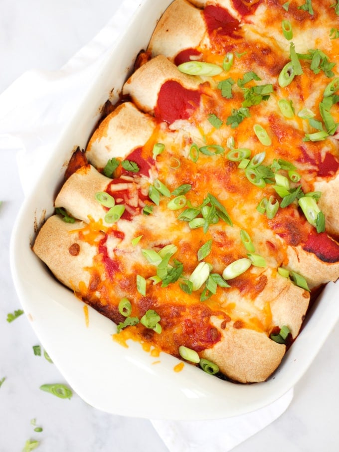 Overhead photo of chicken enchiladas in a white rectangular dish with tomato sauce, cheese melted, onions (scallions) and coriander (cilantro) for easy chicken enchiladas recipe which is also slimming world friendly.