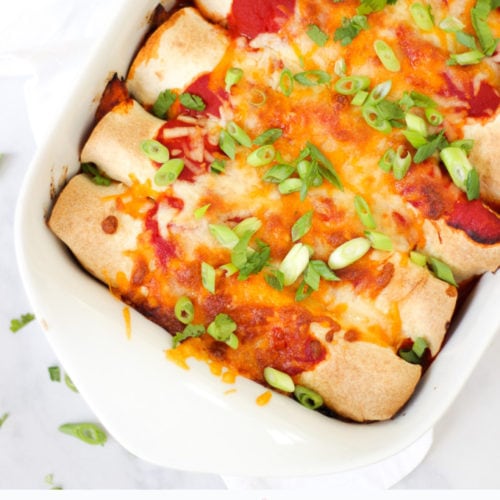 Overhead photo of chicken enchiladas in a white rectangular dish with tomato sauce, cheese melted, onions (scallions) and coriander (cilantro) for easy chicken enchiladas recipe which is also slimming world friendly.