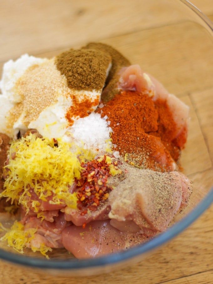 Overhead shot of a glass bowl with ingredients for chicken kebab recipe in, chicken, lemon, paprika, cumin.