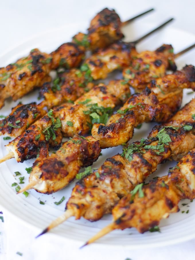 Side photo of chicken kebabs sprinkled with mint. Chicken kebabs lying on a white plate.