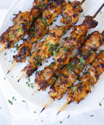 Overhead photo of chicken kebabs on bamboo skewers on white plate.