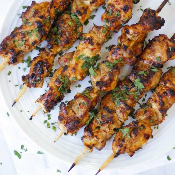 Overhead photo of chicken kebabs on bamboo skewers on white plate.