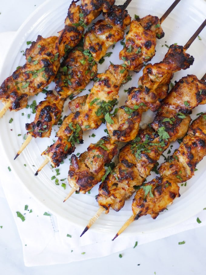 Overhead photo of chicken kebab on bamboo skewers on white plate.