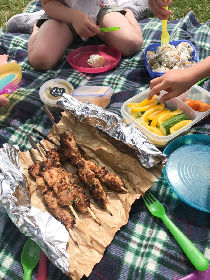 Chicken skewers at a picnic with peppers, tomatoes and a tartan picnic blanket.
