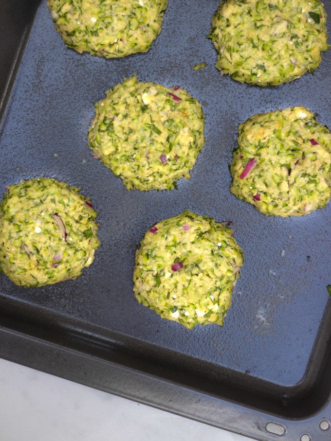 Overhead shot of uncooked patties of courgette fritter recipe batter on a baking sheet.