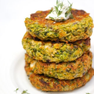 Stack of 4 courgette fritters in a pile side angle photo topped with yoghurt and dill.