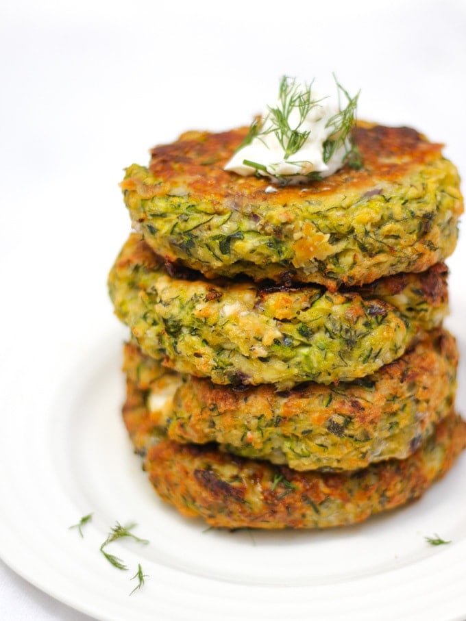 Stack of 4 courgette fritters in a pile side angle photo topped with yoghurt and dill.