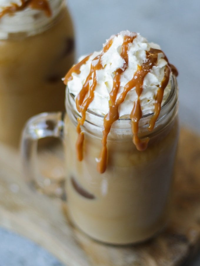  A glass kilner mug of iced coffee, topped with whipped cream and a salted caramel drizzle