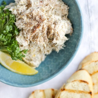 Pile of Smoked Mackerel pate in a green bowl with cress and a wedge of lemon with bread slices in the background on a white napkin. Overhead view photo.