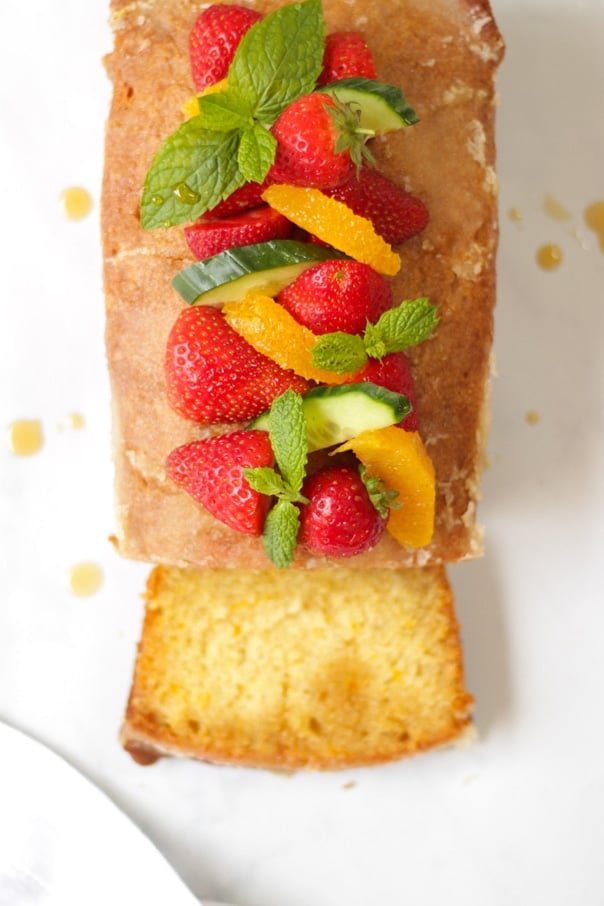 This deliciously moist Orange Drizzle Cake is so easy to make. Loaded with a Pimms drizzle and piles of fruit, it's a must make summer bake. This Pimms Cake is an easy Loaf Cake perfect for parties, afternoon tea or dessert. This is the cake version of your favourite summer cocktail drink! Topped with Strawberries, Cucumber, Mint and Oranges, what could be more delicious?! #pimms #pimmscake #orangecake #loafcake #tamingtwins