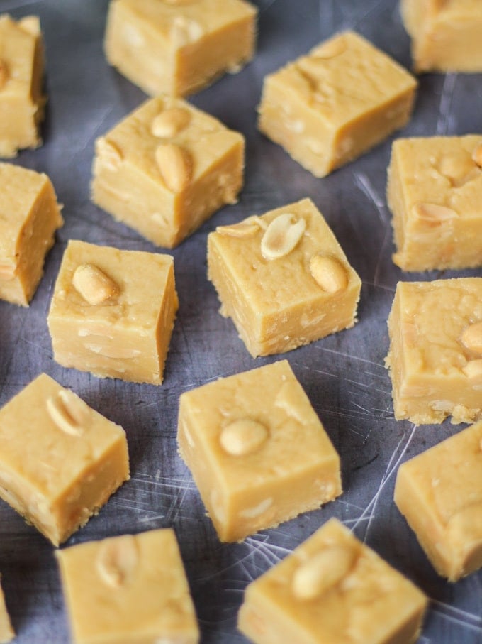 Overhead angled photo of microwave peanut butter fudge cubes with salted peanuts on top on grey background.